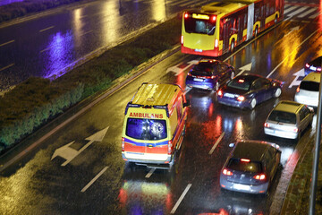 Karetka medyczna ratunkowa w deszczu na sygnale jedzie  na sygnale jedzie wieczorem z pomocą - obrazy, fototapety, plakaty