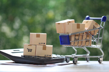 Brown parcel box on model miniature cart with calculator on natural green background, Shopping and Increase taxes concept