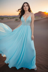 Fototapeta na wymiar Full body portrait of young model in long sky blue dress with wind hem in desert at sunrise