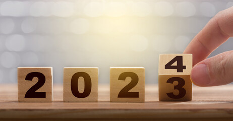 New year exchange concept. Man fingers with turning the calendar wooden block from 2023 to 2024. Figures of the year 2024 on a wooden block. Graphic banner work for the year ending and starting.
