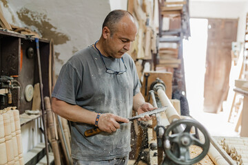 Focused adult ethnic woodworker standing and using tool on rolling machine in workshop