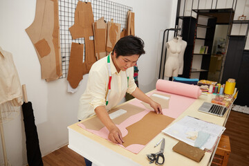 Concentrated female designer in casual clothes preparing pattern on fabric while working at table...
