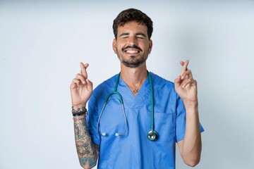 young caucasian doctor man wearing blue medical uniform has big hope, crosses fingers, believes in good fortune, smiles broadly. People and wish concept