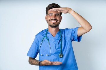 young caucasian doctor man wearing blue medical uniform gesturing with hands showing big and large size sign, measure symbol. Smiling looking at the camera.