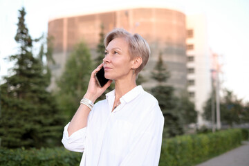 Business Woman With Phone Near Office. Portrait Of Beautiful senior Female In Fashion Office Clothes Talking On Phone While Standing Outdoors. Phone Communication.