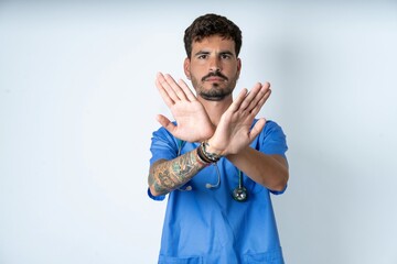 young caucasian doctor man wearing blue medical uniform has rejection expression crossing arms and...