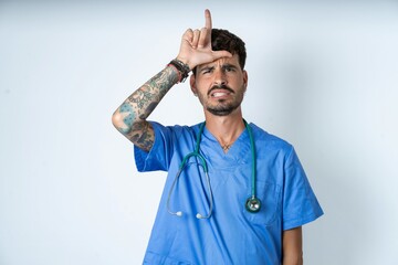 young caucasian doctor man wearing blue medical uniform making fun of people with fingers on...