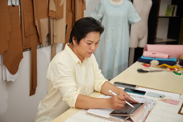 Obraz na płótnie Canvas Seamstress working in tailor shop using tablet