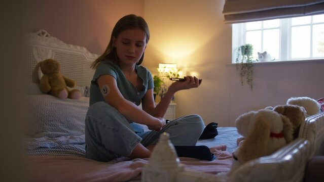 Teenage girl sitting on bed at home injecting herself with insulin pen as treatment for diabetes