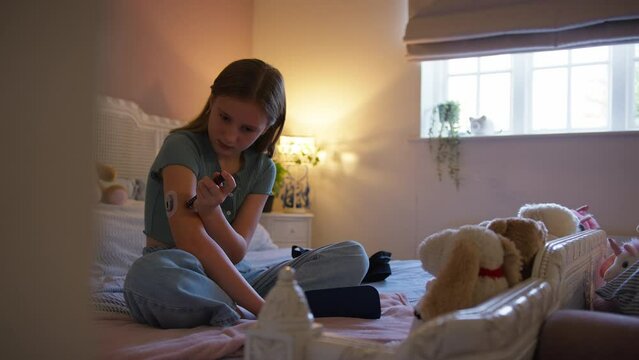 Teenage girl sitting on bed at home injecting herself with insulin pen as treatment for diabetes