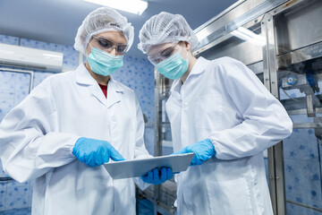 Female worker using tablet checking quality drinking water before process of filling water into plastic bottles to bring out to consumers. Water bottles on production line of factory.