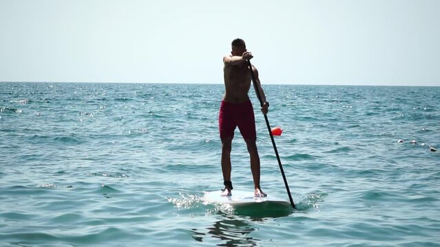 Man Sup Sea. Strong athletic man learns to paddle sup standing on board in open sea ocean on sunny day. Summer holiday vacation and travel concept. Aerial view. Slow motion