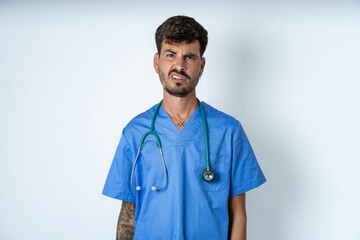 Portrait of dissatisfied young caucasian doctor man wearing blue medical uniform smirks face,...