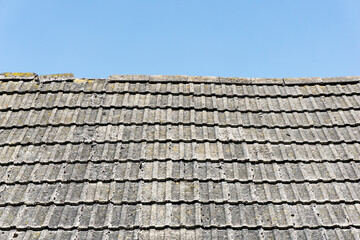 Concrete roof tiles. Old style architecture. Countryside house roof. Tiles texture. Weathered, grunge rooftop. Exterior pattern. Blue sky above roof.
