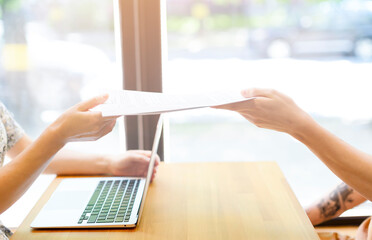 Hands in close-up pass documents to each other above the table with the laptop. Business work,...