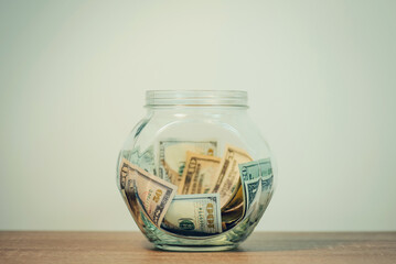 Toned photo of glass jar with saved dollar banknotes. Saving money from the salary or wages to by...
