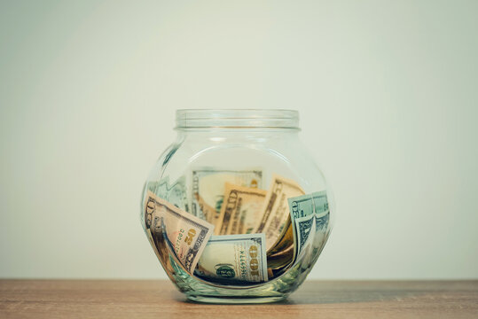 Toned photo of glass jar with saved dollar banknotes. Saving money from the salary or wages to by something big