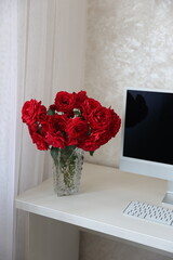 beautiful red roses on the desktop near the computer. roses from my mother's garden. fluffy red roses stand in a vase on the table