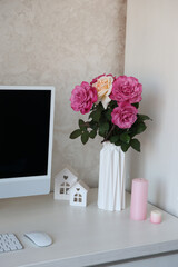 beautiful pink roses stand on the desktop near the computer. roses from my mother's garden. pink roses stand in a white vase on the table and pink candles. workplace and pink roses