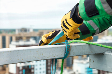 Closeup of male hands industrial mountaineer climber in work uniform with rope equipment on roof building. Access worker high-rise rope dangerous job. Industry urban works concept. Copy ad text space