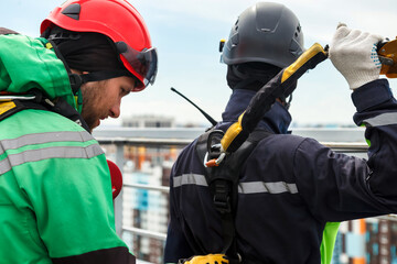 Access climbers high-rise dangerous job. Men industry mountaineer workers in work uniform, checks...