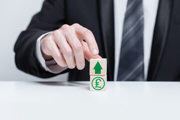 Wooden blocks with green currency pound sterling icon and green arrow up. Growth and depreciation concept.