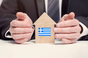 Businessman hand holding wooden home model with Greek flag. insurance and property concepts