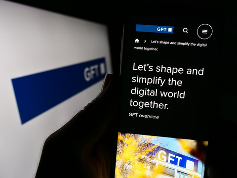 Stuttgart, Germany - 08-21-2023: Person holding smartphone with webpage of German IT company GFT Technologies SE on screen in front of logo. Focus on center of phone display.