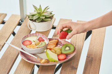 Unrecognizable person taking strawberry from plate with yogurt and fruits