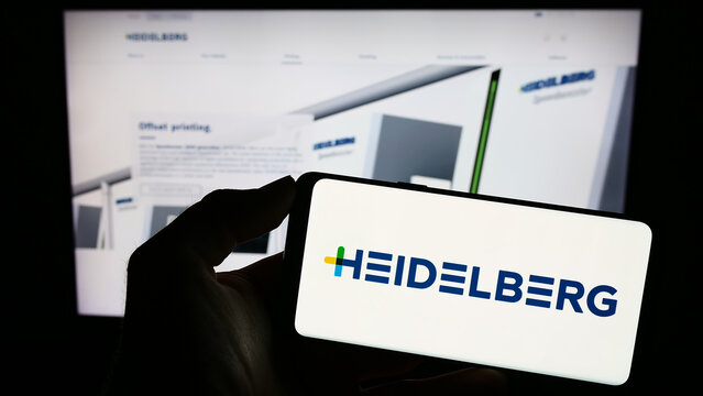 Stuttgart, Germany - 08-22-2023: Person holding mobile phone with logo of German company Heidelberger Druckmaschinen AG on screen in front of web page. Focus on phone display.