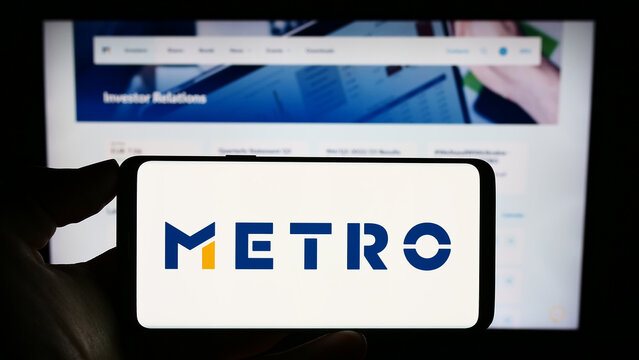 Stuttgart, Germany - 08-22-2023: Person holding cellphone with logo of German wholesale company Metro AG on screen in front of business webpage. Focus on phone display.