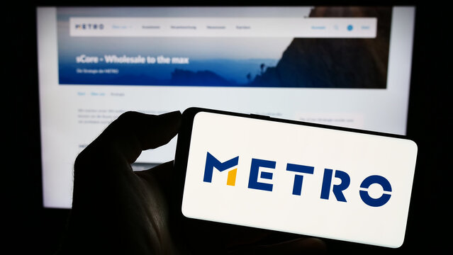 Stuttgart, Germany - 08-22-2023: Person holding smartphone with logo of German wholesale company Metro AG on screen in front of website. Focus on phone display.