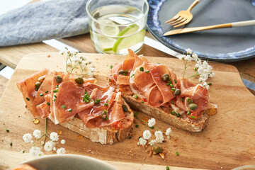 Delicious bruschettas with prosciutto and water glass served on table