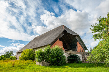 Fototapeta premium View of abandoned barn and dynamic sky. Weathered and worn red barn on an abandoned farm. Latvia.