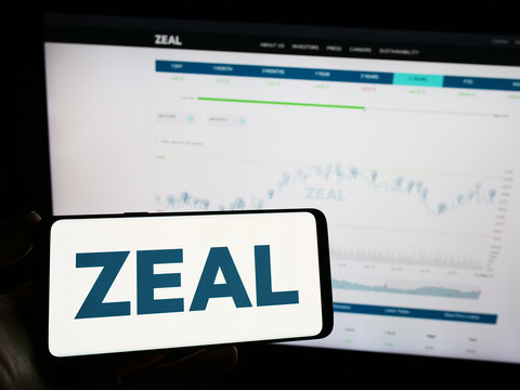 Stuttgart, Germany - 08-24-2023: Person holding mobile phone with logo of German lottery company ZEAL Network SE on screen in front of business web page. Focus on phone display.