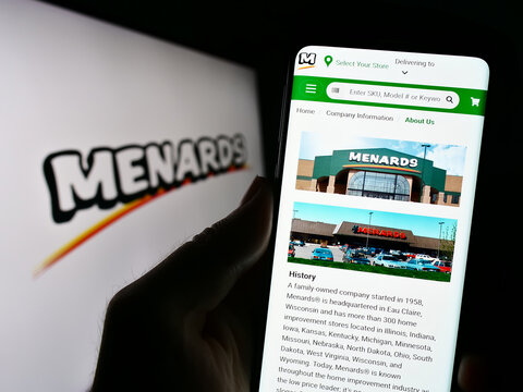 Stuttgart, Germany - 08-24-2023: Person holding cellphone with website of US retail company Menard Inc. (Menards) on screen in front of logo. Focus on center of phone display.