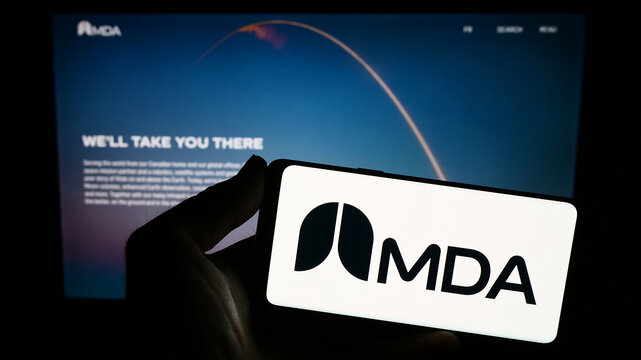 Stuttgart, Germany - 08-25-2023: Person holding smartphone with logo of Canadian space technology company MDA Ltd. on screen in front of website. Focus on phone display.