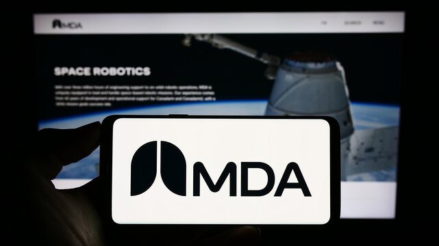 Stuttgart, Germany - 08-25-2023: Person holding cellphone with logo of Canadian space technology company MDA Ltd. on screen in front of business webpage. Focus on phone display.