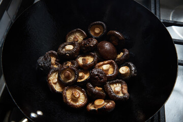 shiitake mushrooms close up frying in wok on stove