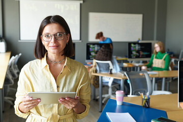 Portrait of teacher in eyeglasses looking at camera while using tablet pc at lesson