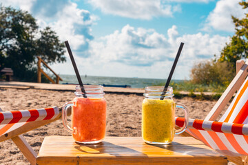 Two fruity cocktails in jar with deep red and green color.cocktails on luxury tropical beach.Blurred sea sky and vacationers background.