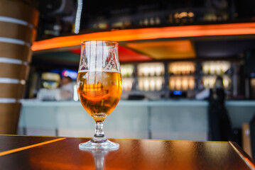 A beer in Tulip glass. Glass of light beer on wooden table in cafe or restaurant .Beautiful crystal glass with golden freshly brewed cold wheat beer stands on table cafe,restaurant terrace.