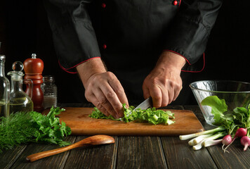 Cutting vegetables with a knife in the hands of a cook for cooking vegetarian food. Fresh vegetable food on the kitchen table