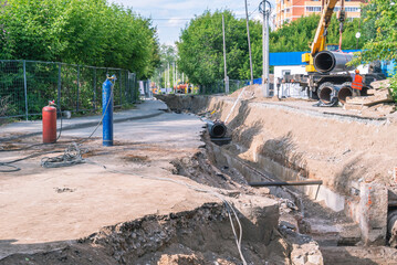 Trench and replacement of an outdated heat supply pipeline. A cylinder with oxygen and propane for gas welding. The crane unloads new large heat supply pipes. Earthworks. Construction site.