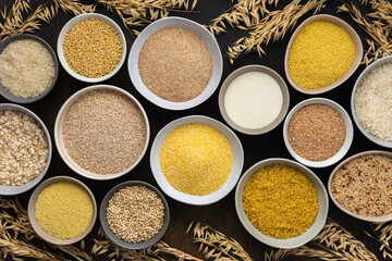 Various grain cereals in bowls, top view on a brown background with bowls of cereals and ears of oats