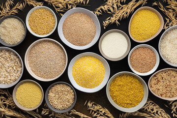 Various grain cereals in bowls, top view on a brown background with bowls of cereals and ears of...