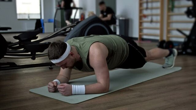 Fat man struggles to do plank exercise at the gym, and then falls exhausted on the mat.