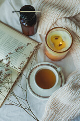 Home decor. Book, knitted blanket, candle, cup of hot tea. Cozy autumn.