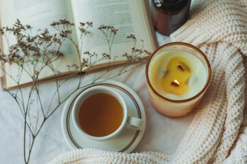 Home decor. Book, knitted blanket, candle, cup of hot tea. Cozy autumn.