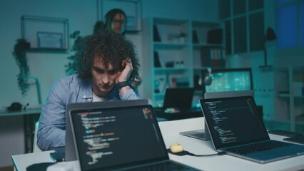 Young man programmer working till late, saying bye to colleague leaving office